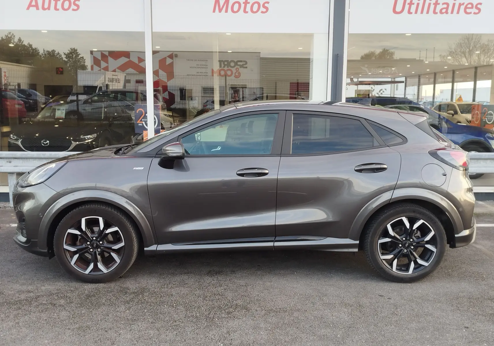 Profil droit d'un Ford Puma 1.0 EcoBoost gris métallisé avec jantes alliage noires et détails sportifs visibles.