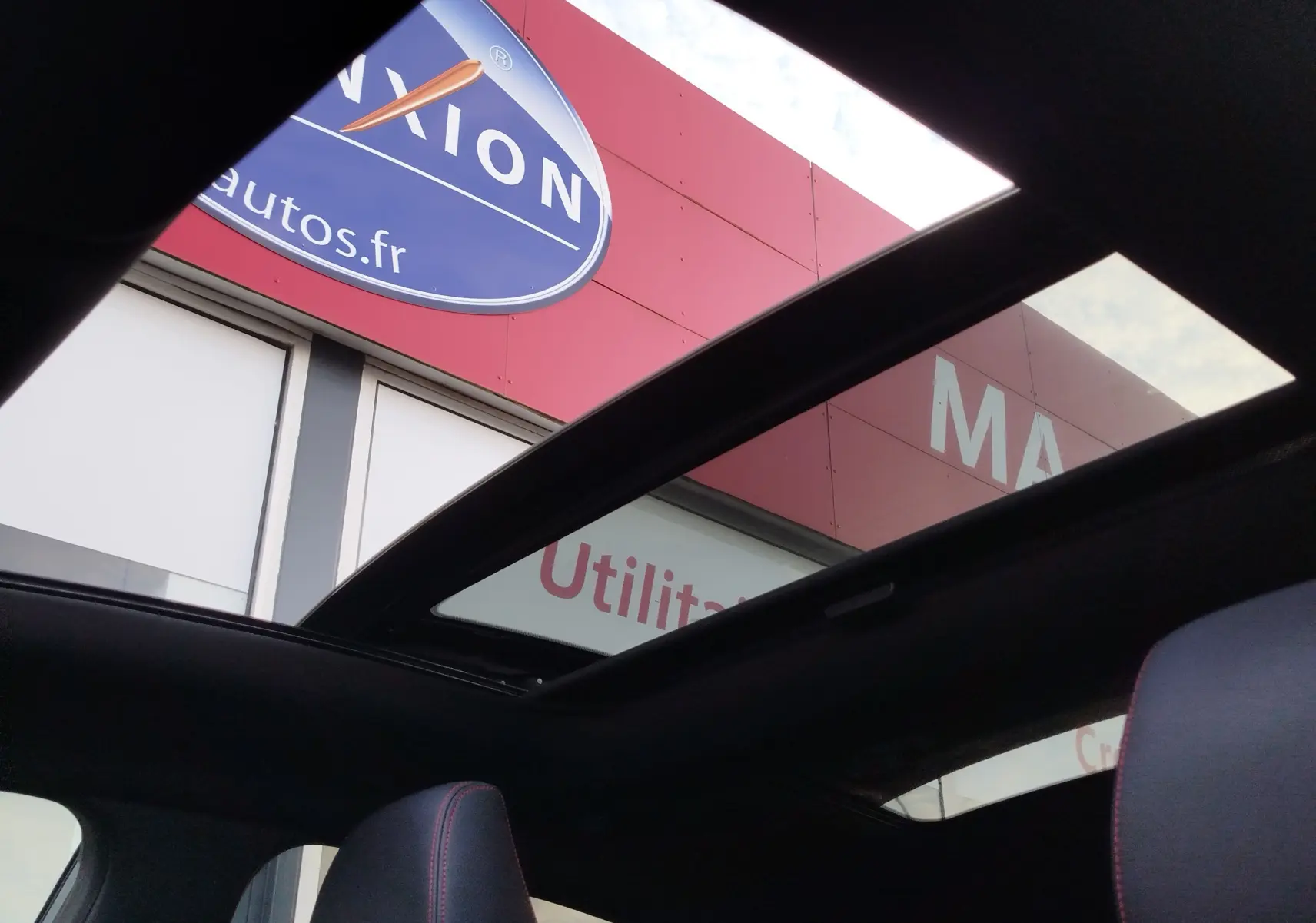 Toit panoramique ouvert vu de l'intérieur du Ford Puma gris Fashion, avec siège avant et ciel visible.