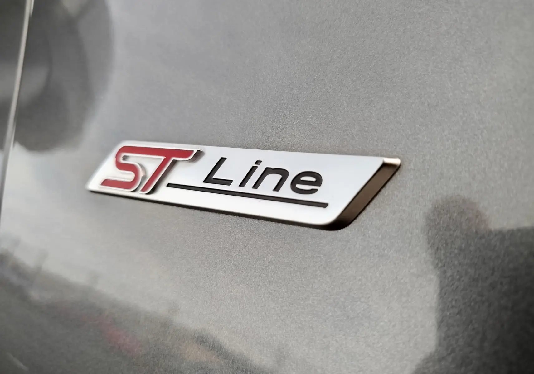 Gros plan sur le logo ST-Line rouge et noir sur la carrosserie gris métallisé d'une Ford Puma 2020.