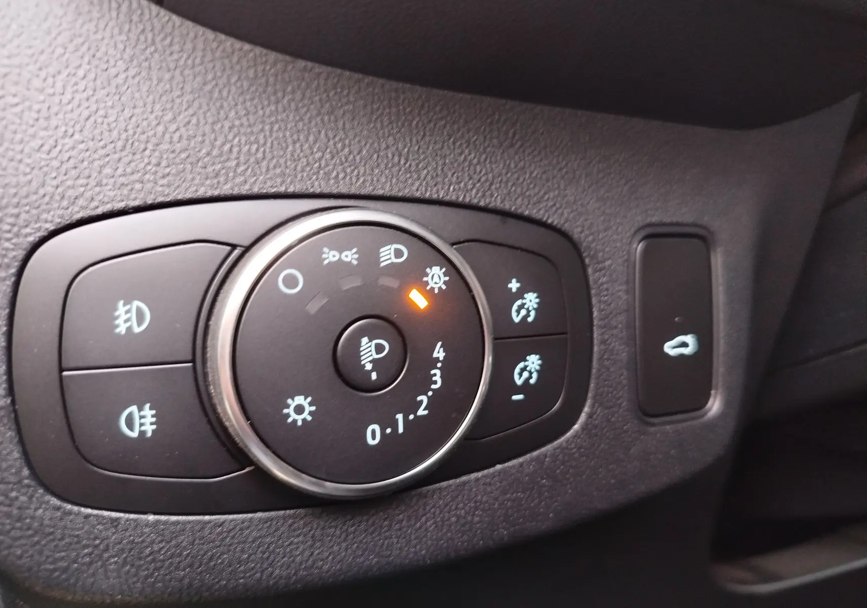 Gros plan sur le bouton de réglage des phares avec témoin orange, intérieur noir du Ford Puma 2020.