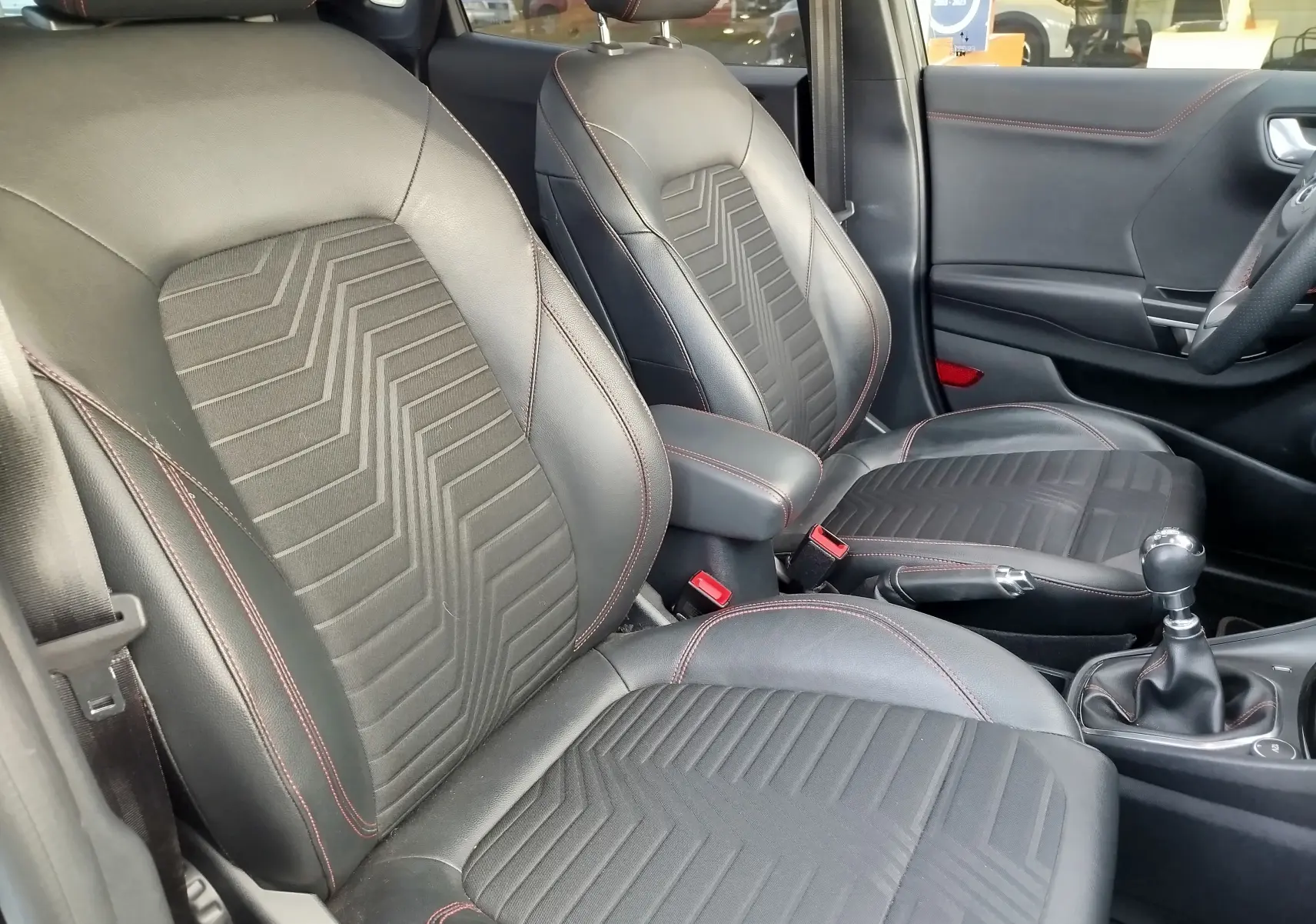 Intérieur avant du Ford Puma 1.0 EcoBoost 2020, sièges noirs avec surpiqûres rouges et levier de vitesse manuel visible.