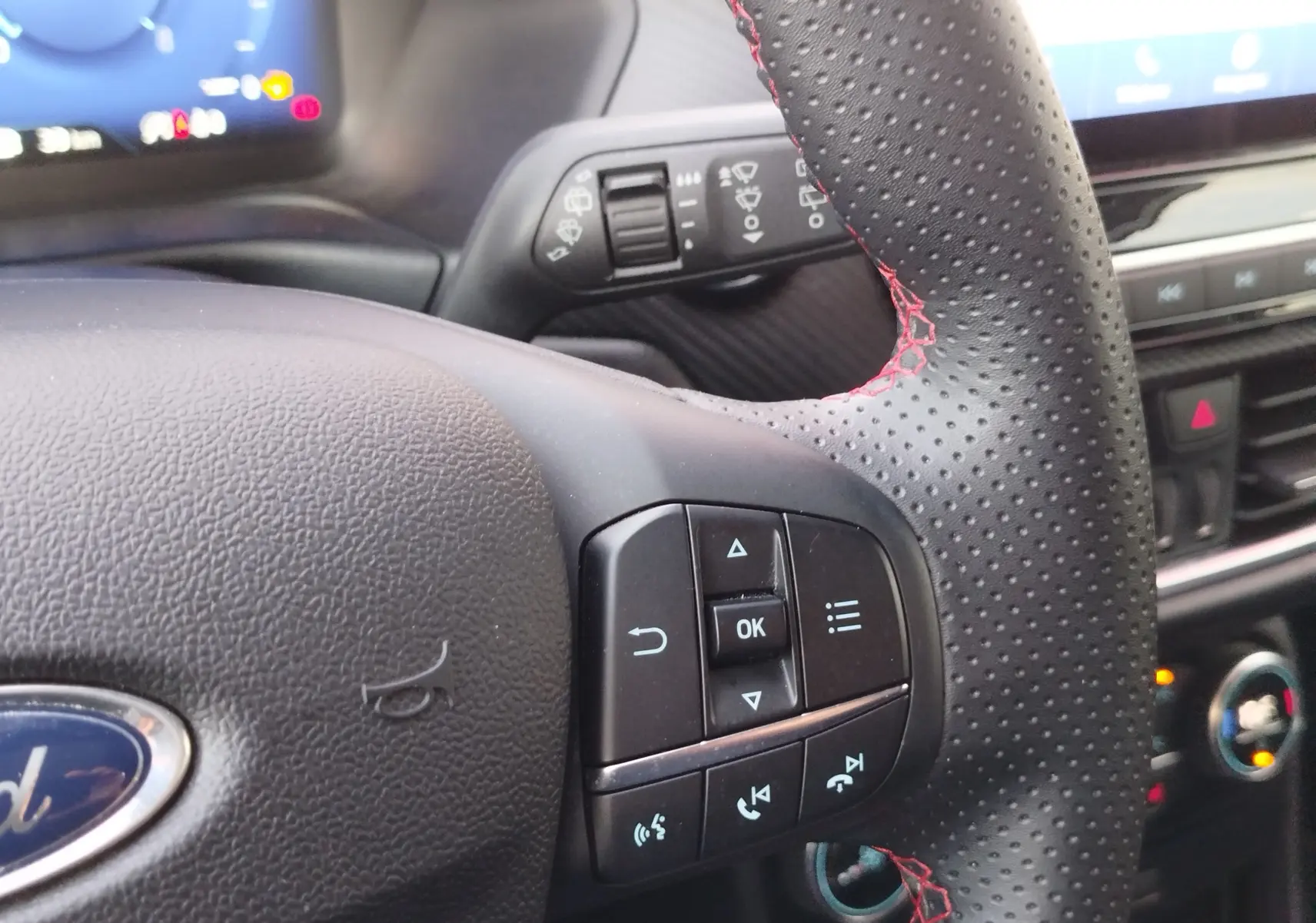 Gros plan sur le volant en cuir perforé avec surpiqûres rouges du Ford Puma 2020, commandes intégrées visibles.