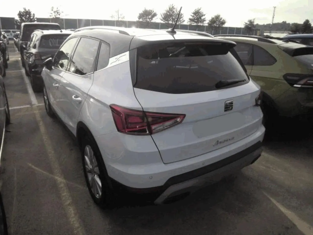 Vue 3/4 arrière d'un SEAT Arona blanc Nevada avec toit noir et feux arrière LED en triangle sur un parking.