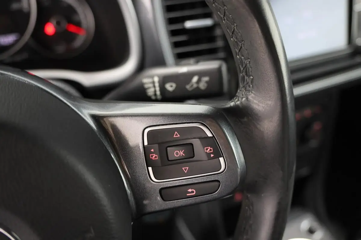 Gros plan sur les commandes au volant en cuir noir du Volkswagen Coccinelle gris, version 2016 avec GPS.