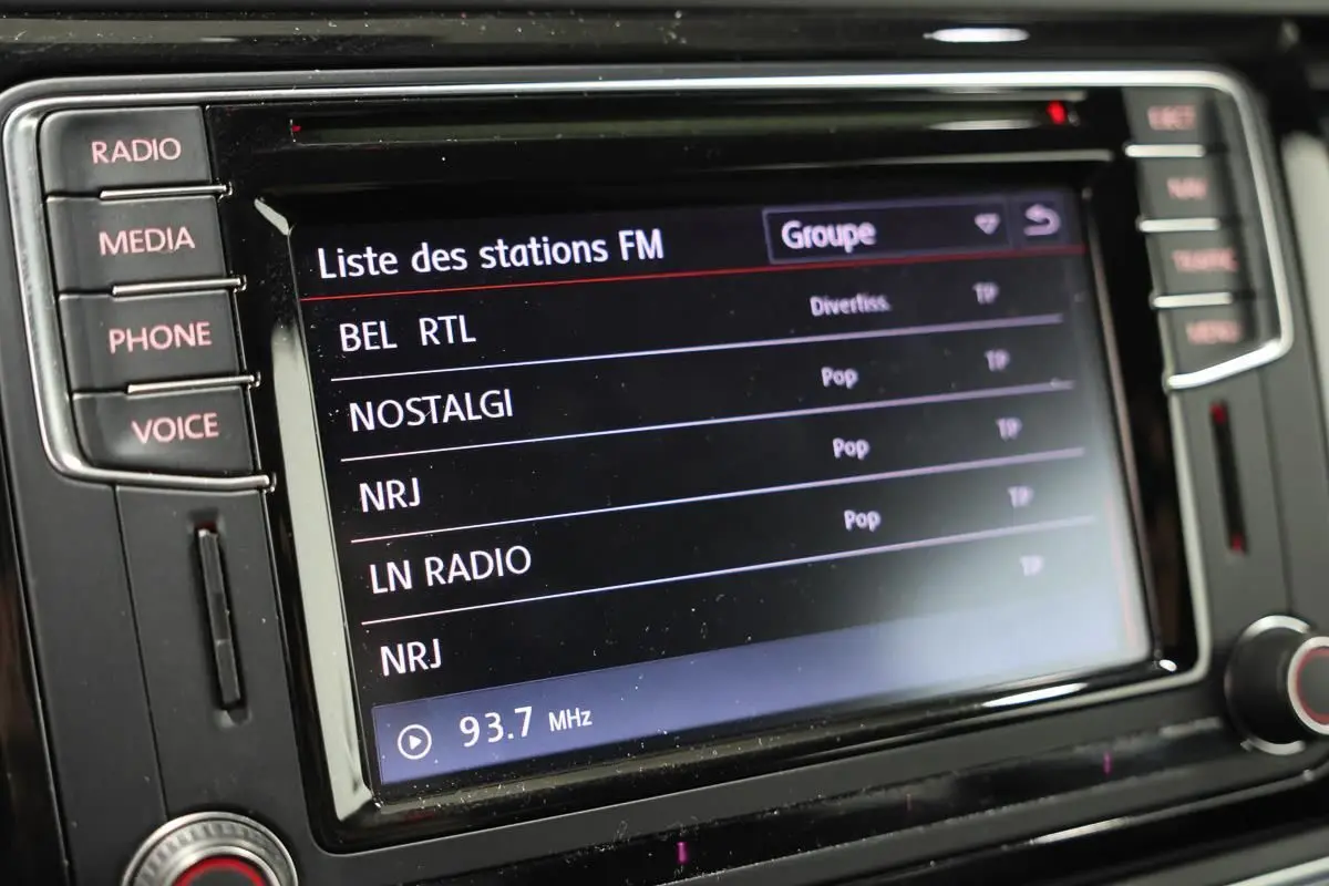 Gros plan sur l’écran central tactile du GPS de la Volkswagen Coccinelle gris, affichant la liste des stations FM.