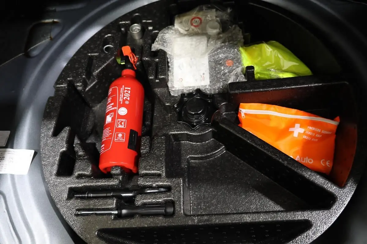 Vue plongeante sur le coffre à outils d’une Volkswagen Coccinelle gris, avec extincteur rouge et trousse de secours orange.