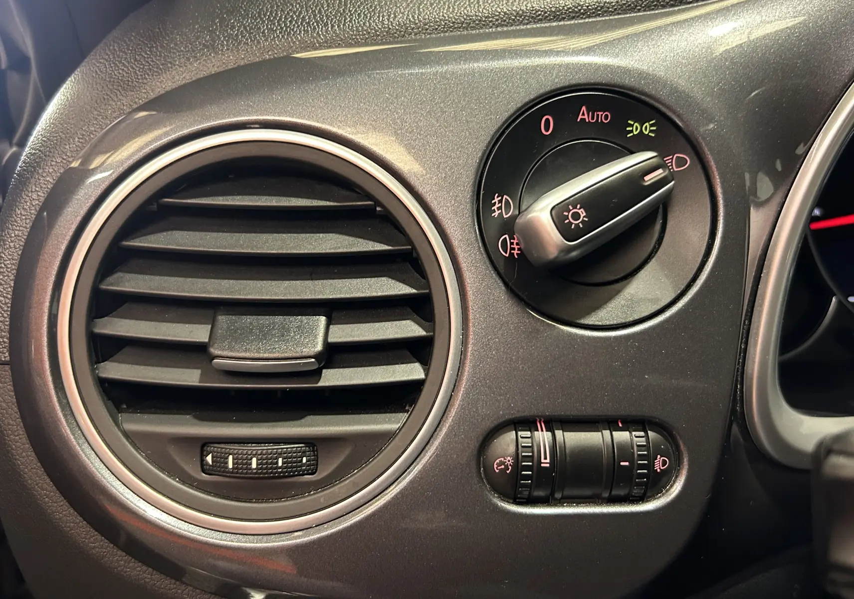 Détail du tableau de bord côté gauche avec la commande des phares et la sortie d'air ronde du Volkswagen Coccinelle gris 2016.