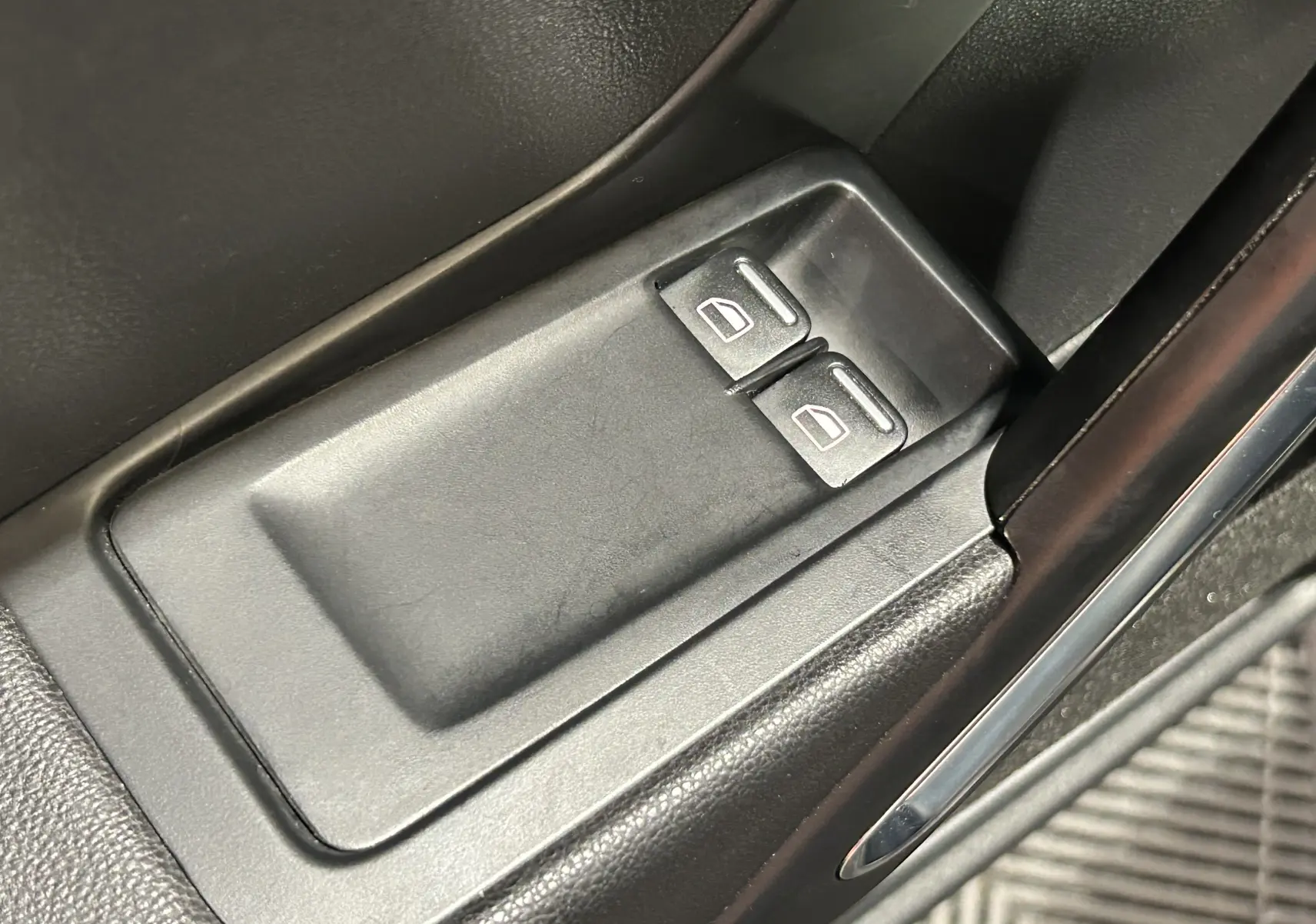 Gros plan sur les commandes de lève-vitres électriques côté conducteur, intérieur noir du Volkswagen Coccinelle gris 2016.