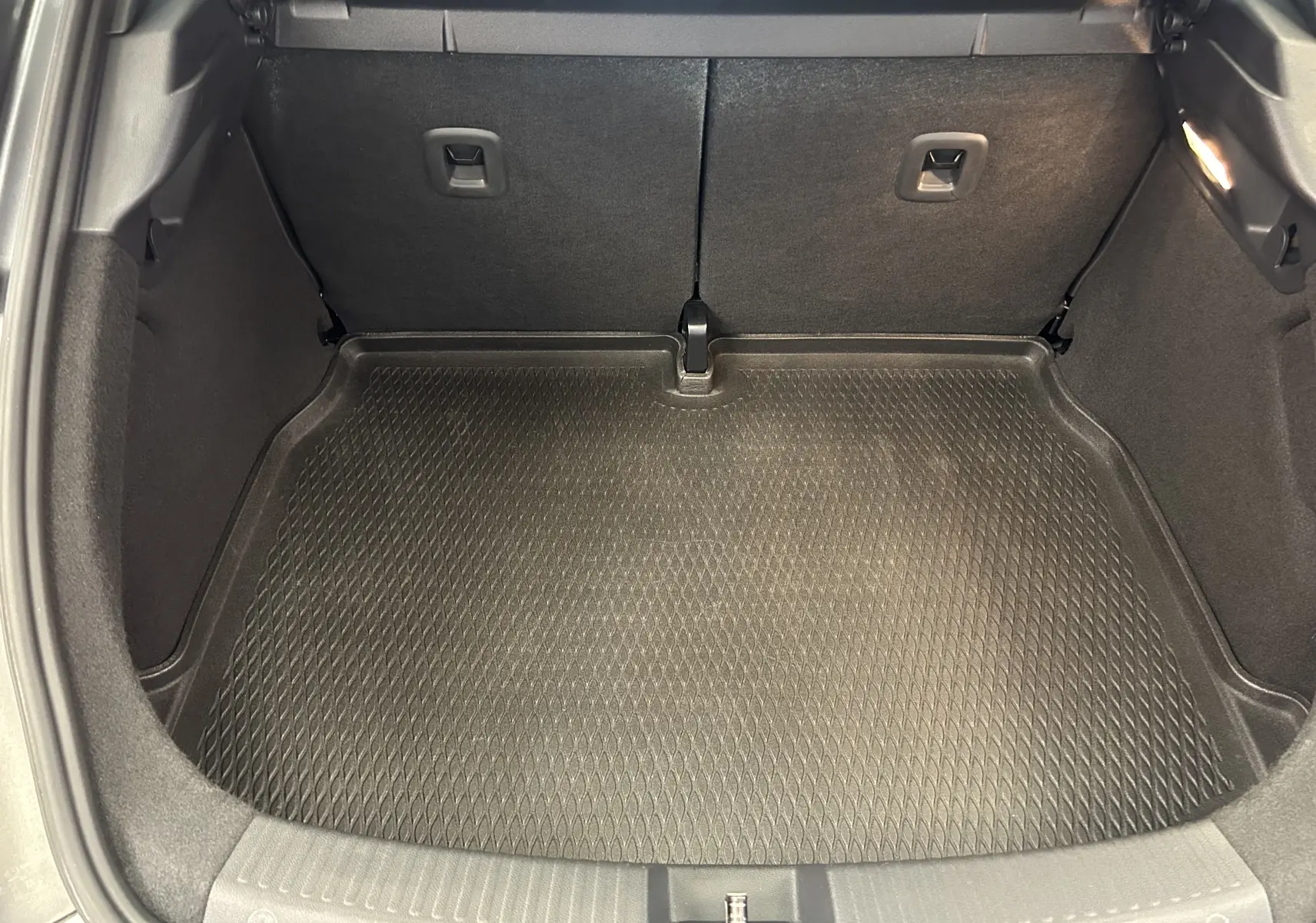 Coffre ouvert vu de l'arrière, tapis de protection noir dans le coffre d'une Volkswagen Coccinelle gris.