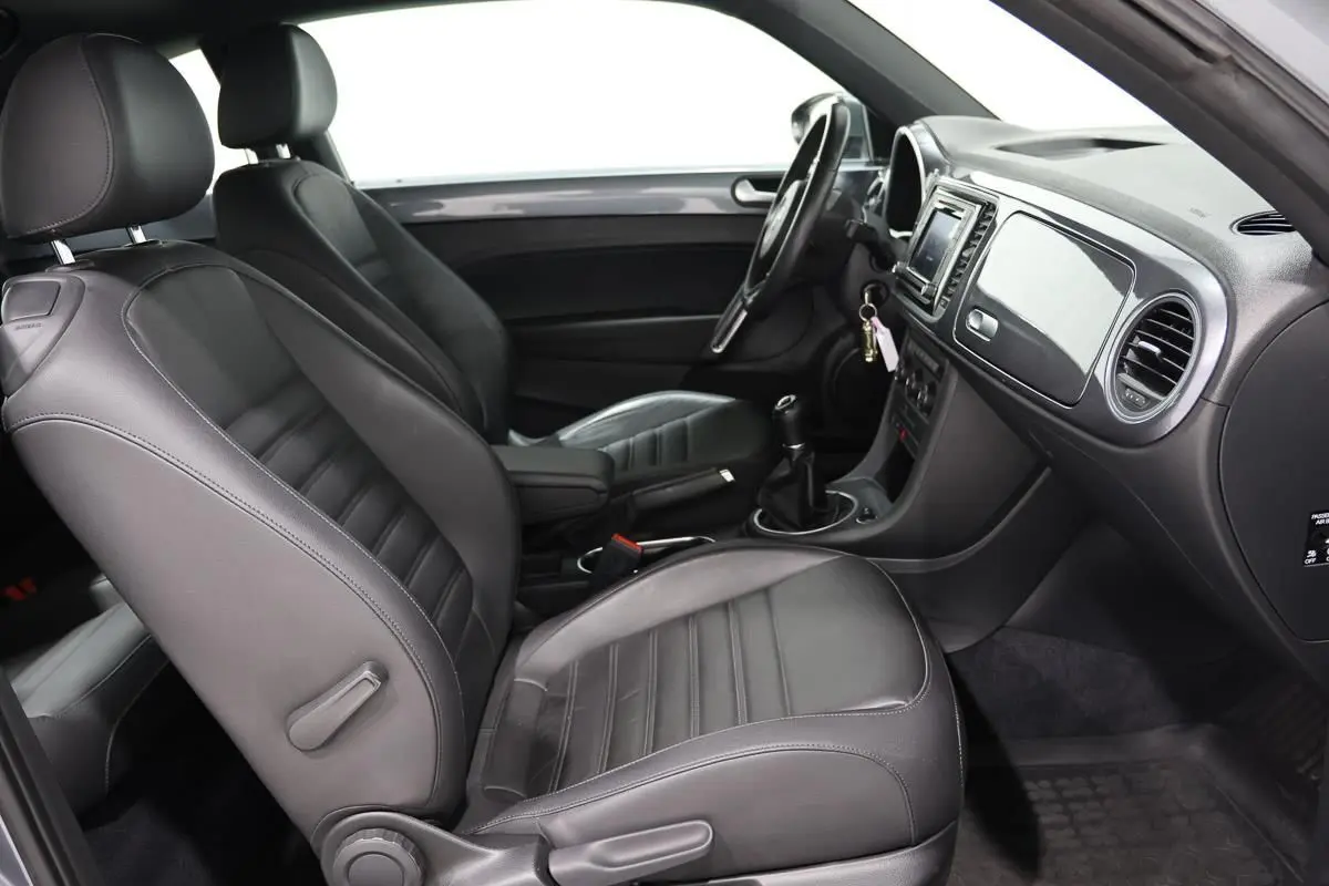 Vue intérieure côté droit de la Volkswagen Coccinelle 2016 avec sièges cuir noirs et tableau de bord équipé d’un GPS.