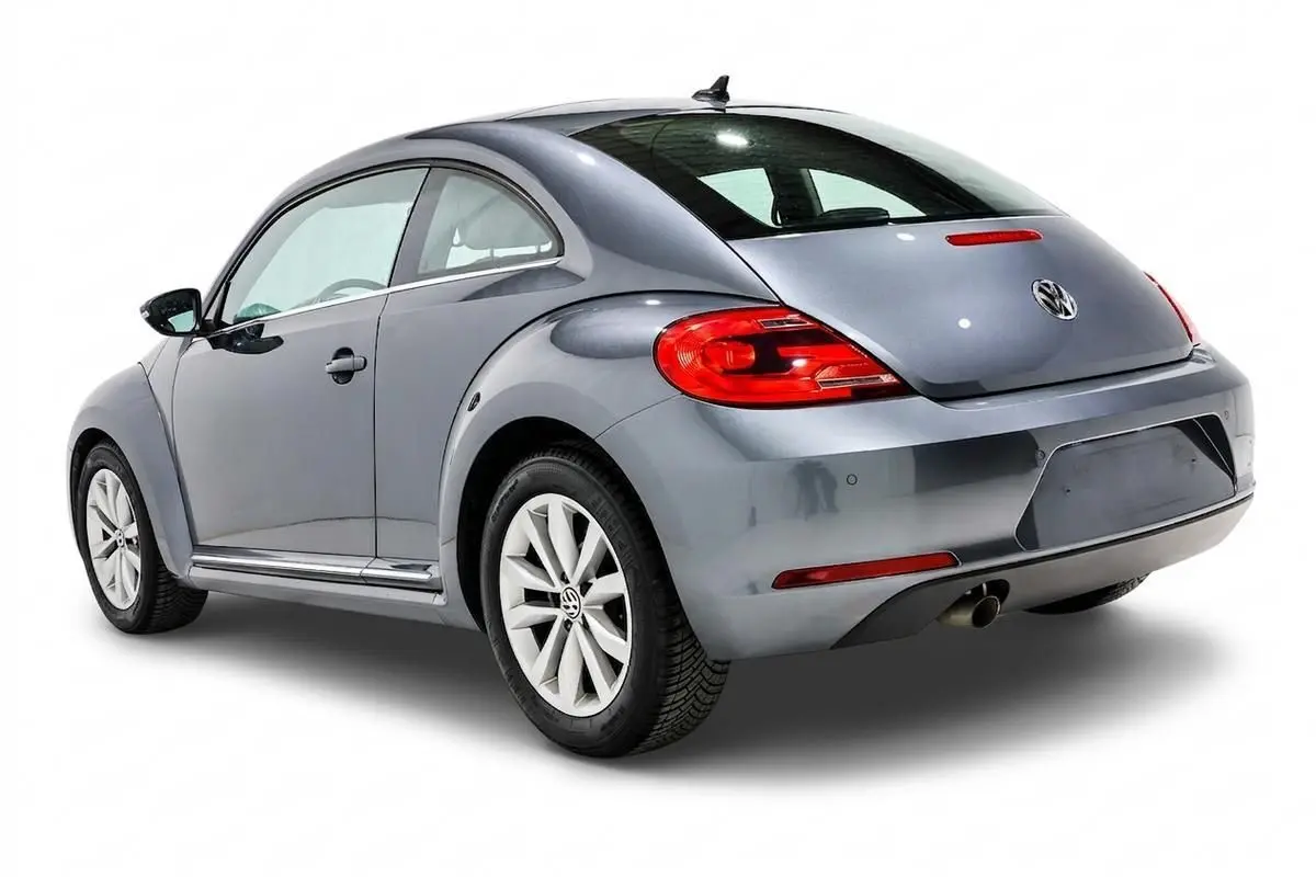 Volkswagen Coccinelle gris vue 3/4 arrière droit, avec feux arrière rouges et jantes alliage blanches.