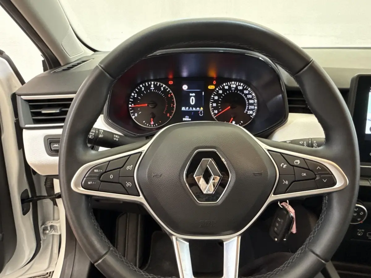 Vue intérieure centrée sur le volant cuir noir de la Renault Clio blanche avec tableau de bord numérique allumé.