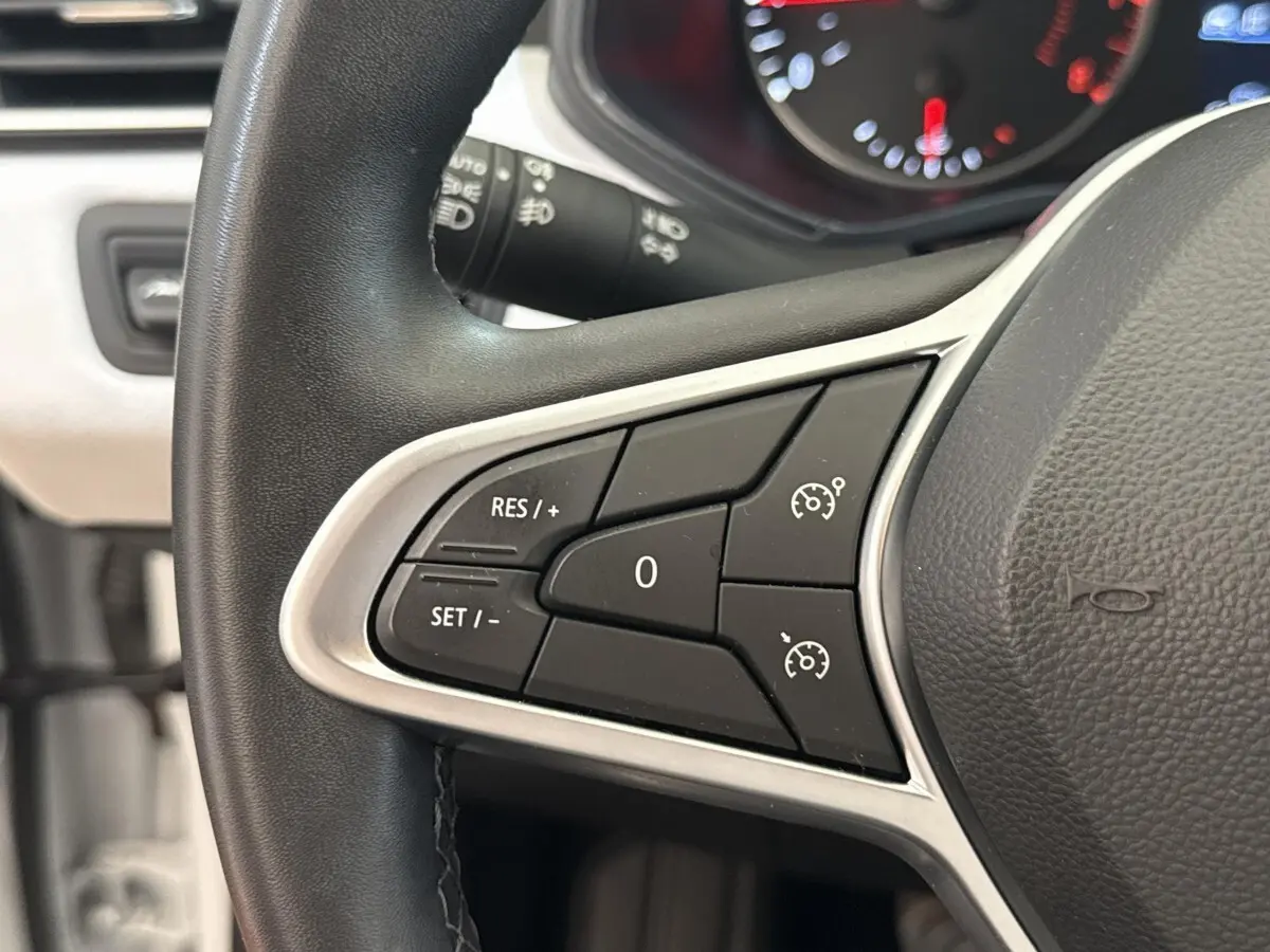 Gros plan sur les commandes du régulateur de vitesse au volant noir de la Renault Clio blanche 2023.