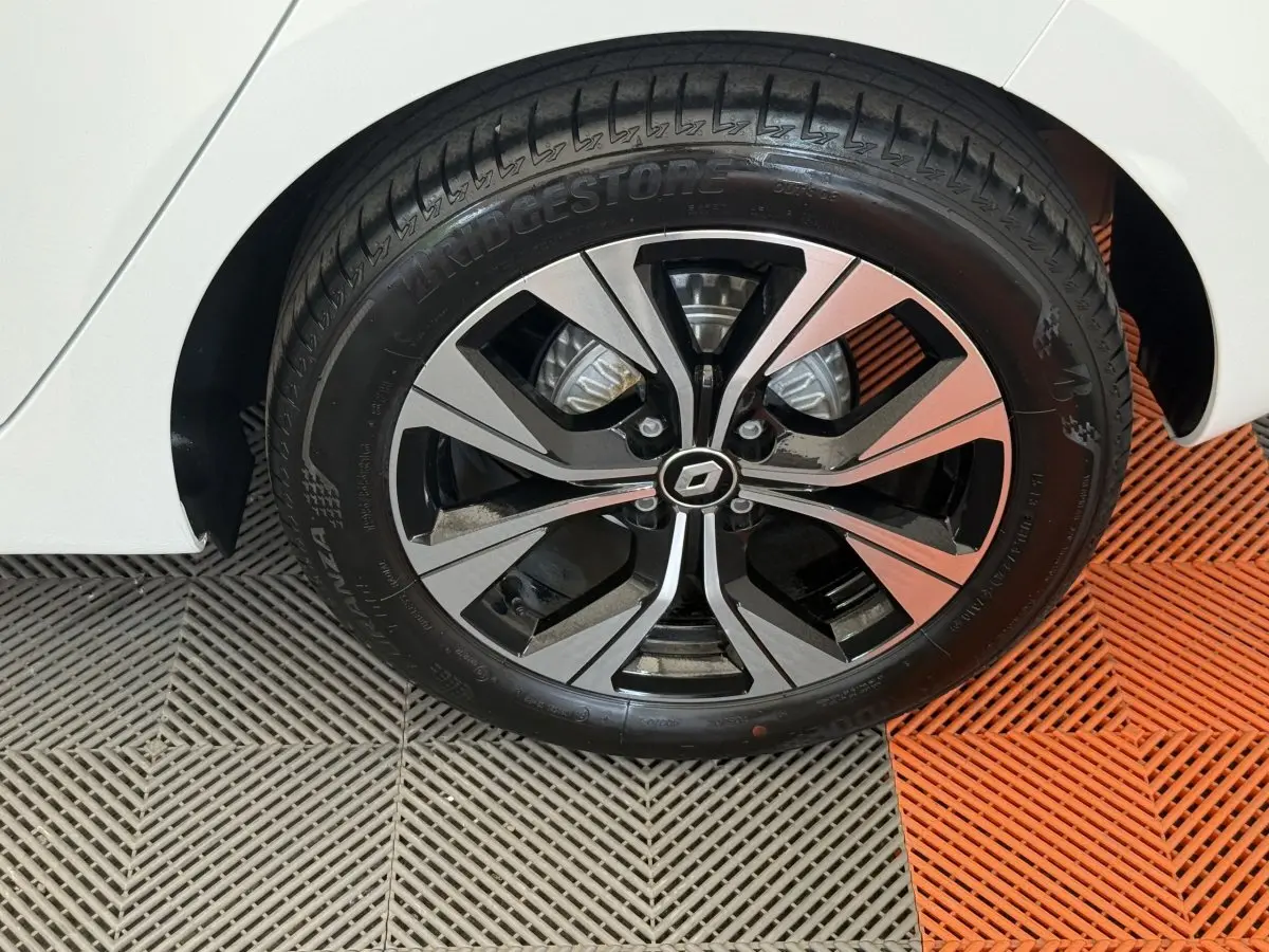 Gros plan sur la roue avant droite d’une Renault Clio blanche, jante alliage noire et argentée au design moderne.