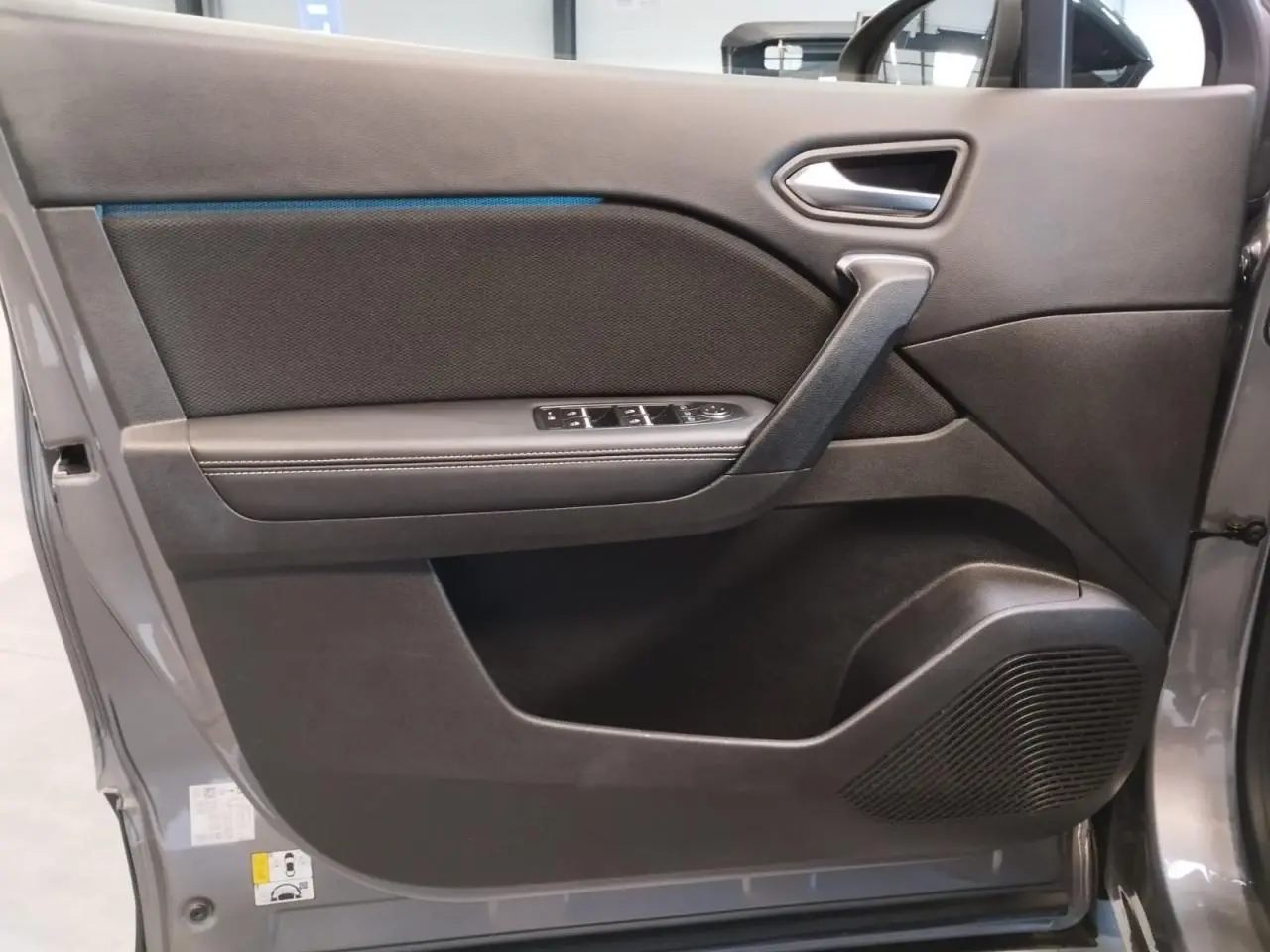 Gros plan sur la porte avant gauche du Renault Symbioz 2025 gris Cassiopée avec commandes de vitres et haut-parleur intégré.