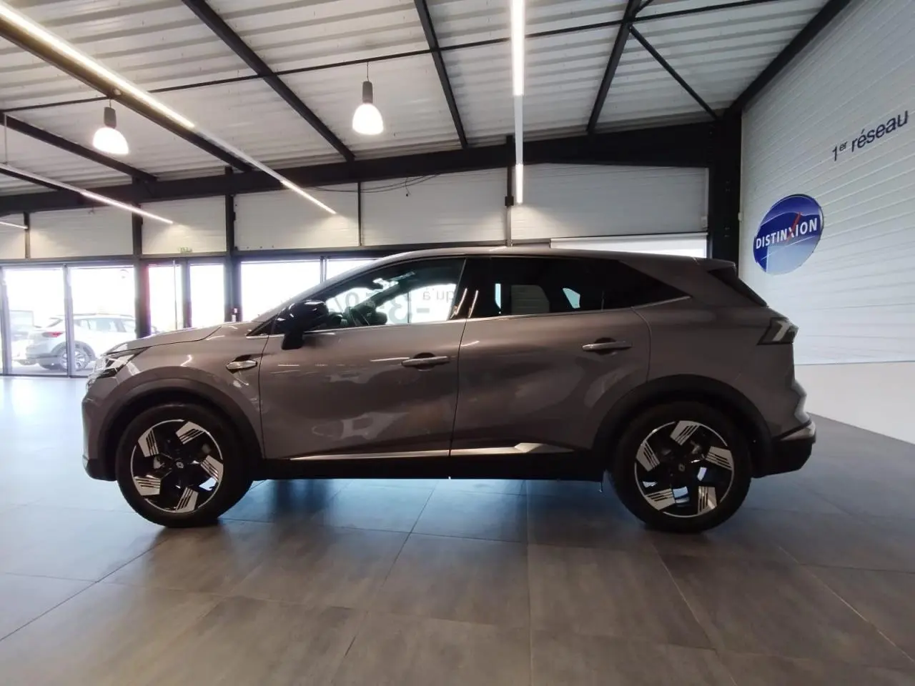 Renault Symbioz 2025 gris Cassiopée vue de profil côté gauche avec jantes 18 pouces Gravity en intérieur showroom.