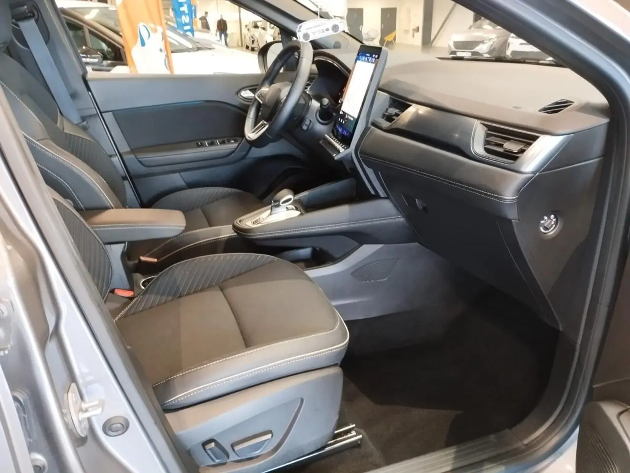 Intérieur avant droit du Renault Symbioz gris Cassiopée, sièges tissu noir et console centrale avec écran vertical tactile.