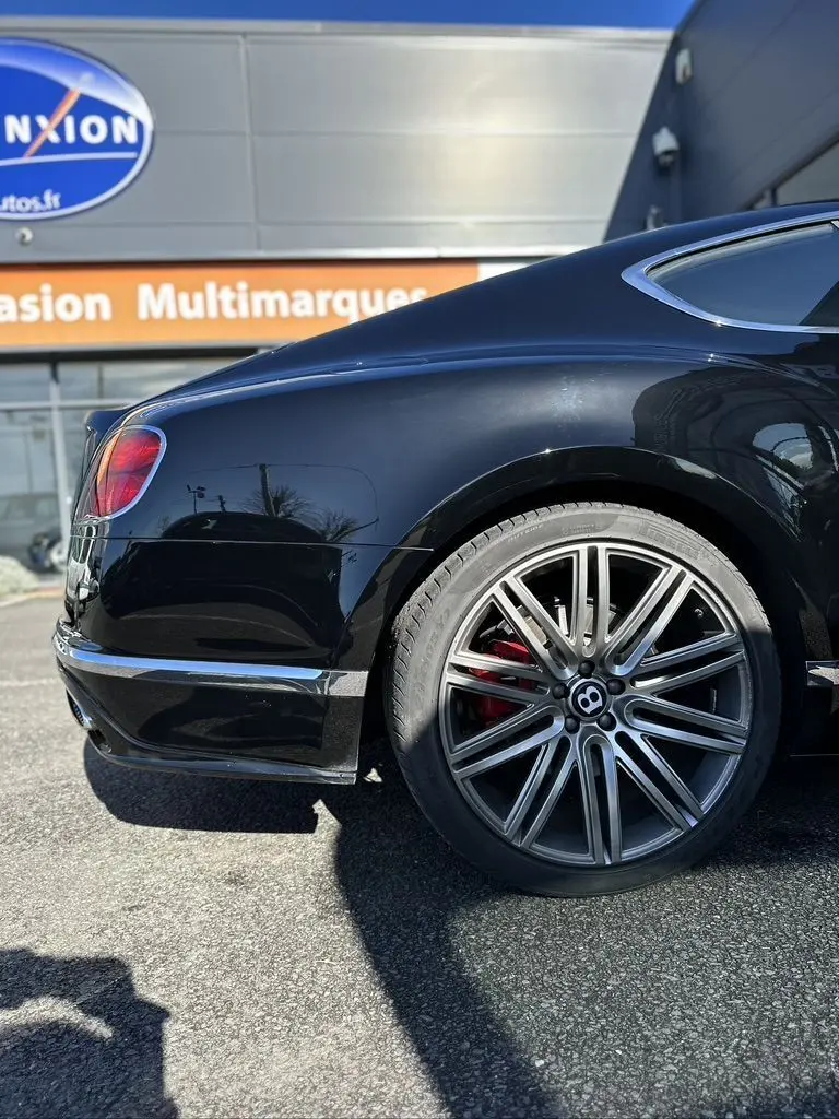 Vue latérale arrière droite d'une Bentley Continental GT Speed noire avec jante alliage et étrier de frein rouge visible.