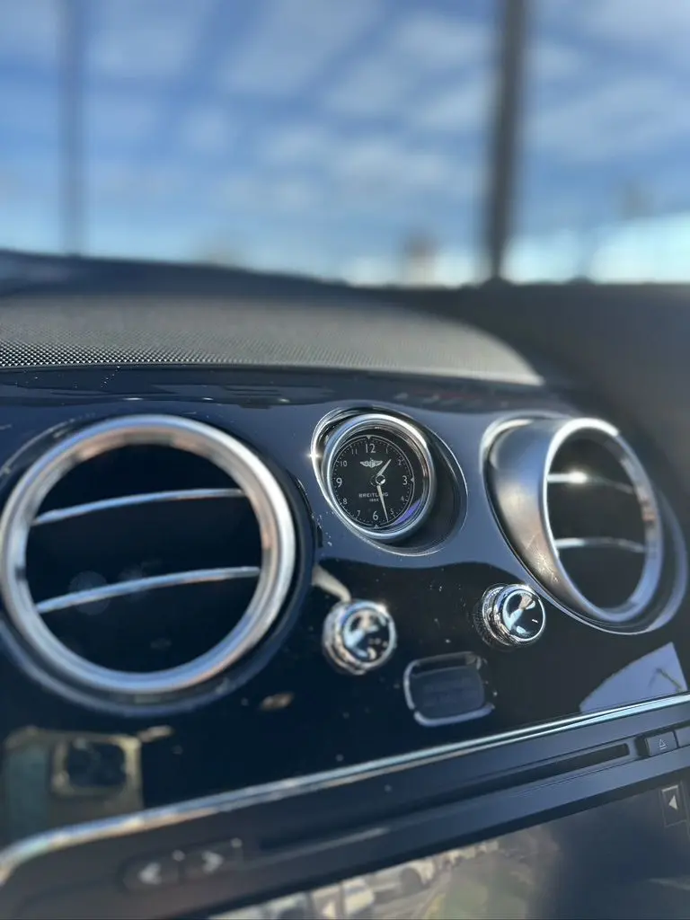 Gros plan sur l'horloge Breitling et les aérateurs chromés du tableau de bord noir d'une Bentley Continental GT Speed 2015.