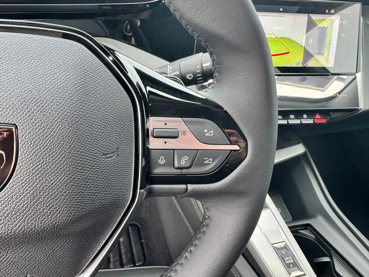 Gros plan sur le volant cuir noir de la Peugeot 308 SW 2024 avec commandes intégrées et écran tactile affichant la caméra de recul.