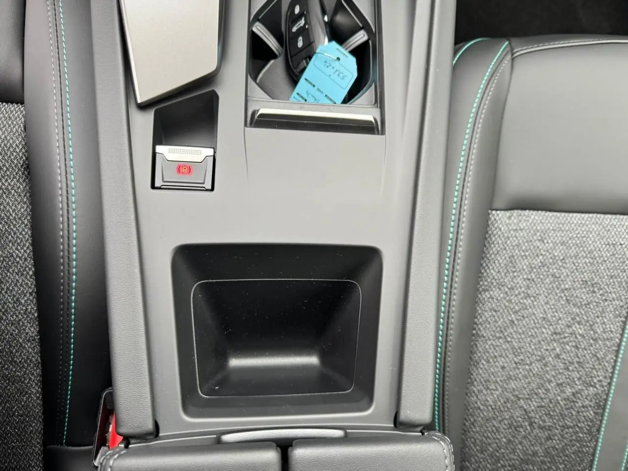 Gros plan sur la console centrale et accoudoir avant en sellerie noire avec surpiqûres bleues du Peugeot 308 SW blanc Okenite 2024