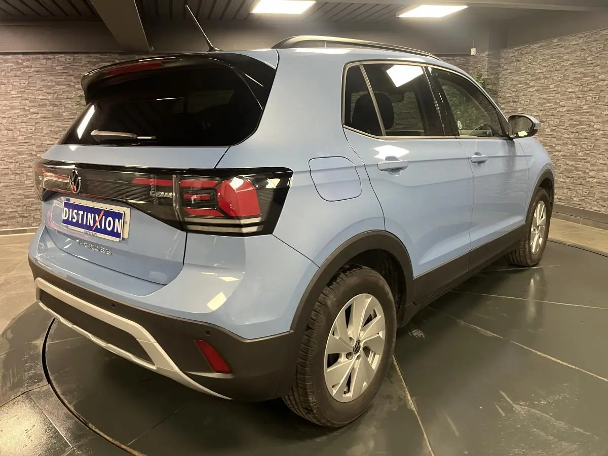 Volkswagen T-Cross bleu clair en 3/4 arrière droit, vitres arrière surteintées et jantes alliage argent.