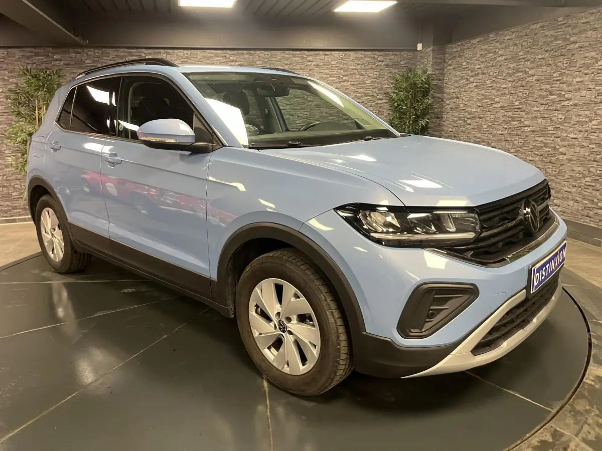 Volkswagen T-Cross bleu clair en 3/4 avant droit, avec vitres arrière surteintées et jantes alliage argent.