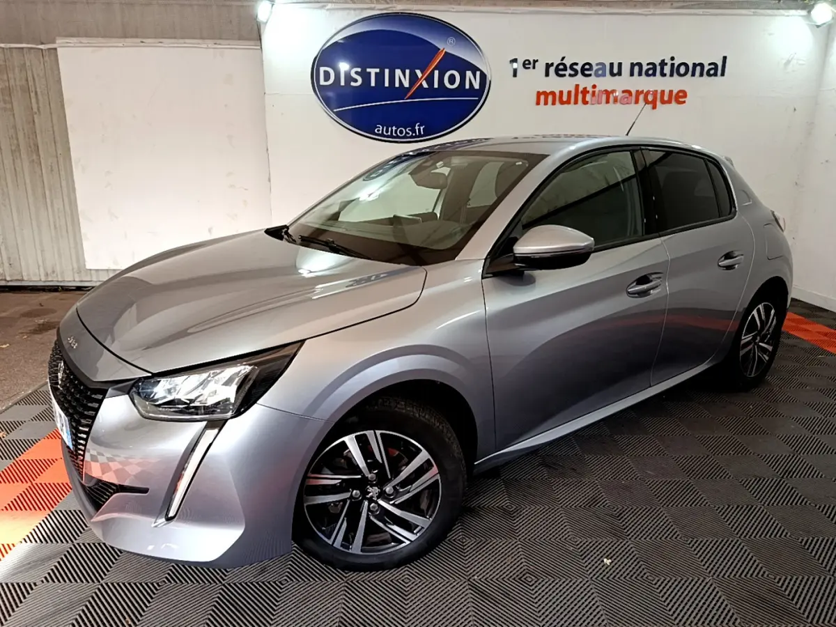 Peugeot 208 gris clair vue 3/4 avant droit dans un showroom avec jantes alliage et phares LED distinctifs.