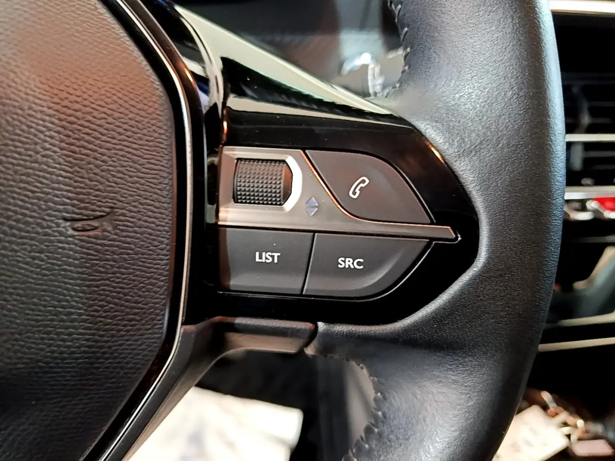 Gros plan sur les commandes gauche du volant cuir noir du Peugeot 208 gris clair, avec boutons LIST, SRC et téléphone.
