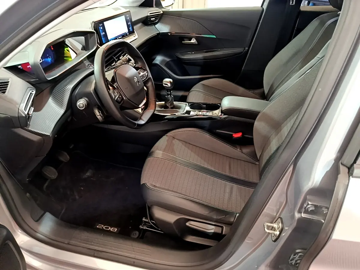 Intérieur côté conducteur d'une Peugeot 208 gris clair, avec tableau de bord numérique et volant cuir multifonctions.