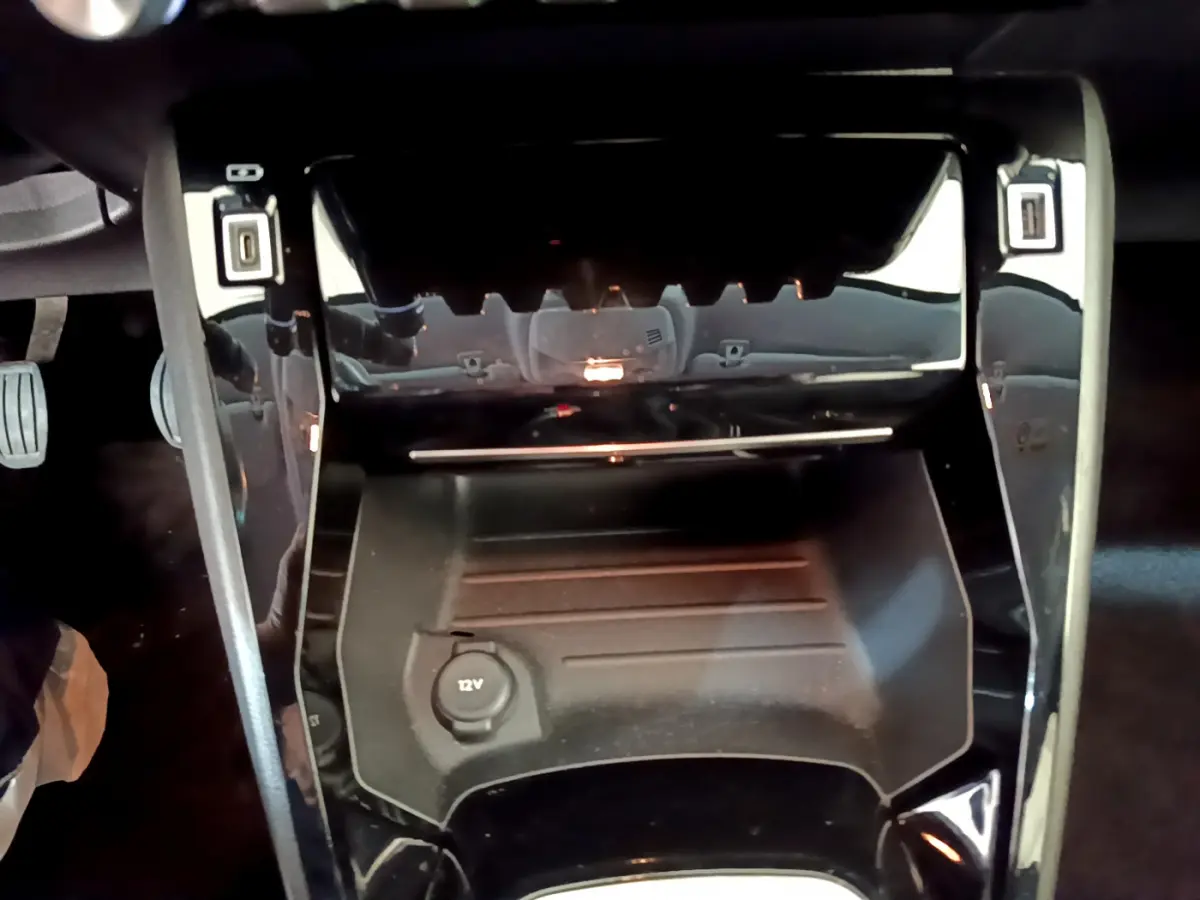 Gros plan sur la console centrale noire de la Peugeot 208 PureTech 100 S&S Allure Business avec prise 12V visible.