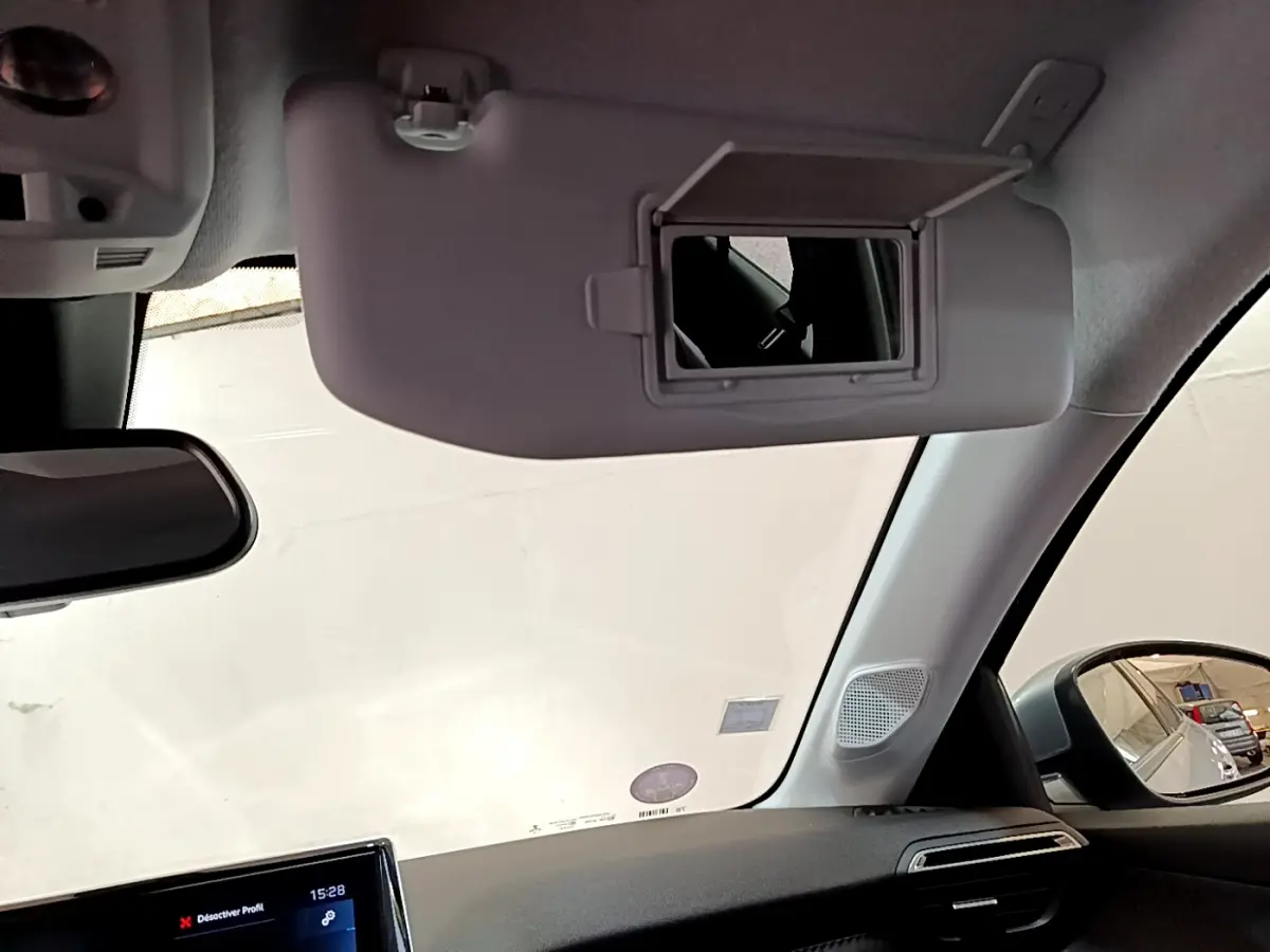 Intérieur du Peugeot 208 gris clair, vue côté passager avec pare-soleil et miroir de courtoisie ouvert.