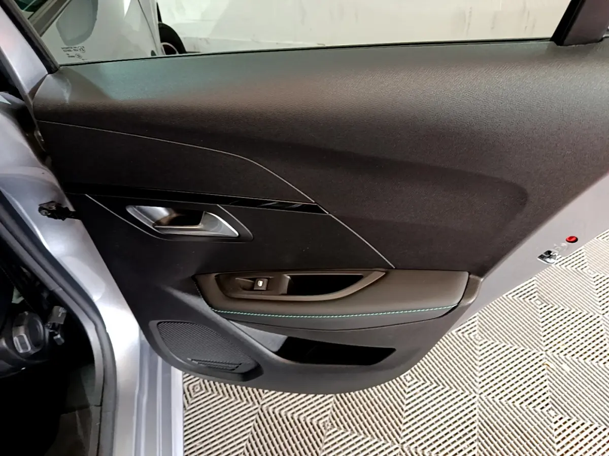 Vue rapprochée de la porte avant gauche gris clair de la Peugeot 208 PureTech 100 S&S Allure Business avec poignée argentée et surpiqûres bleues.