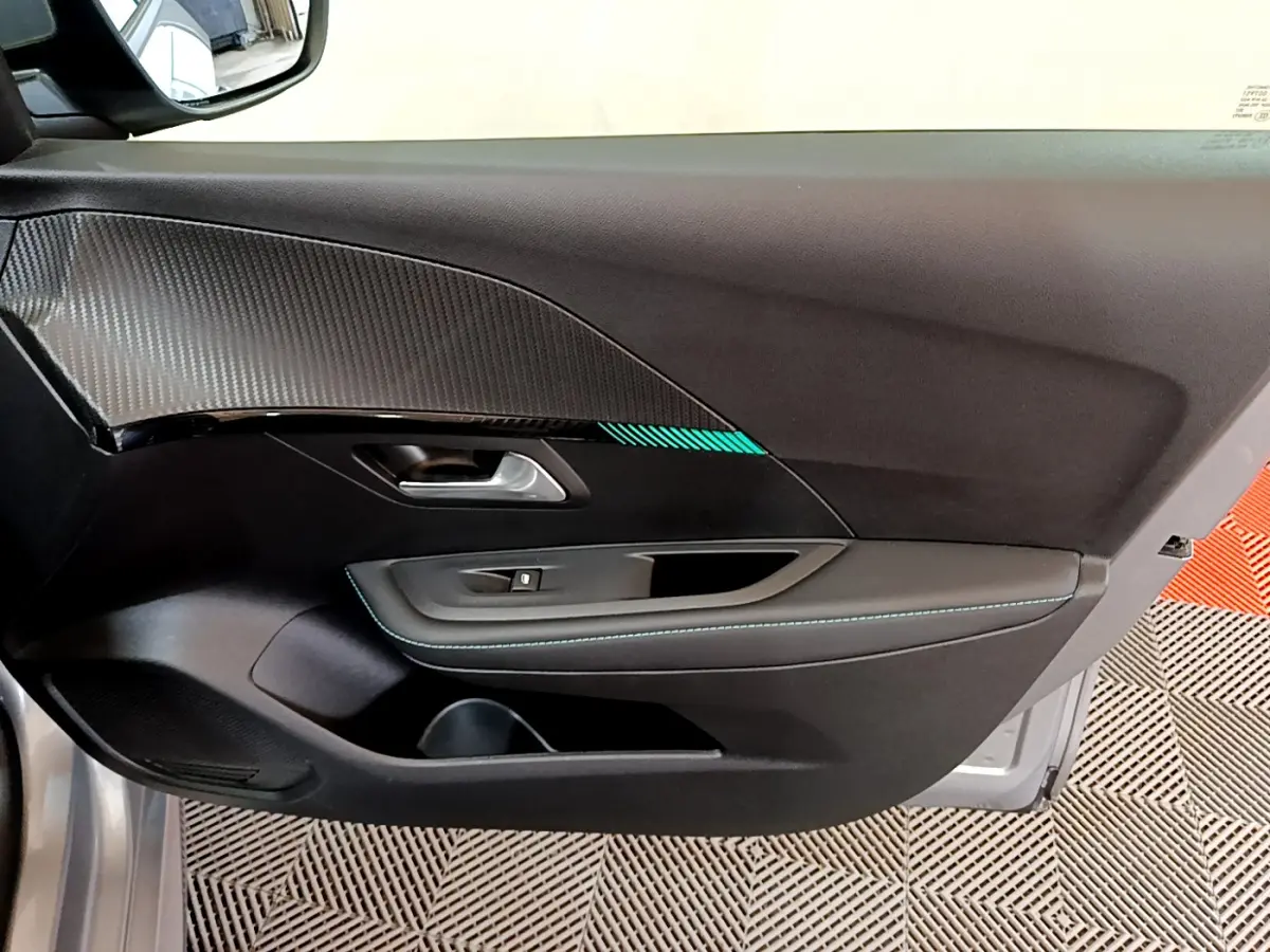 Vue rapprochée de la porte avant gauche gris clair de la Peugeot 208 avec insert décoratif et surpiqûres bleues.