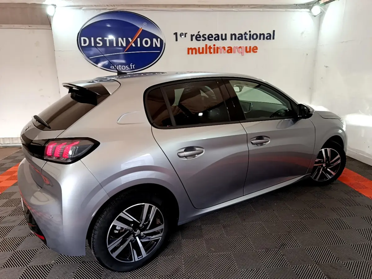 Peugeot 208 gris clair vue 3/4 arrière droit, feux arrière LED et jantes alliage distinctives visibles.
