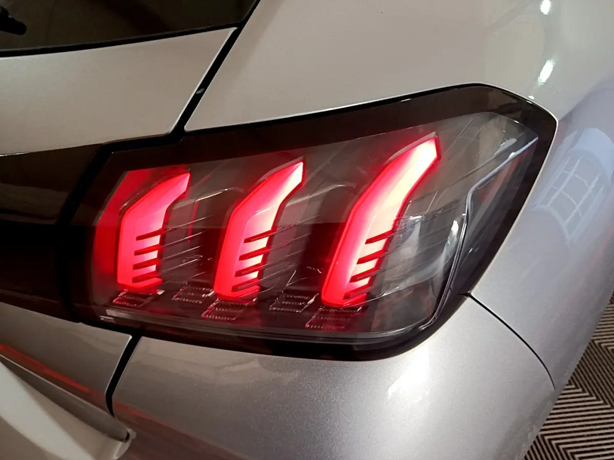 Gros plan sur le feu arrière droit allumé d'une Peugeot 208 gris clair, soulignant son design à trois griffes LED.