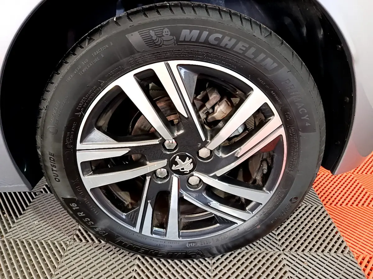 Gros plan sur la roue avant droite de la Peugeot 208 gris clair, jante alliage noire et argent avec logo lion central.