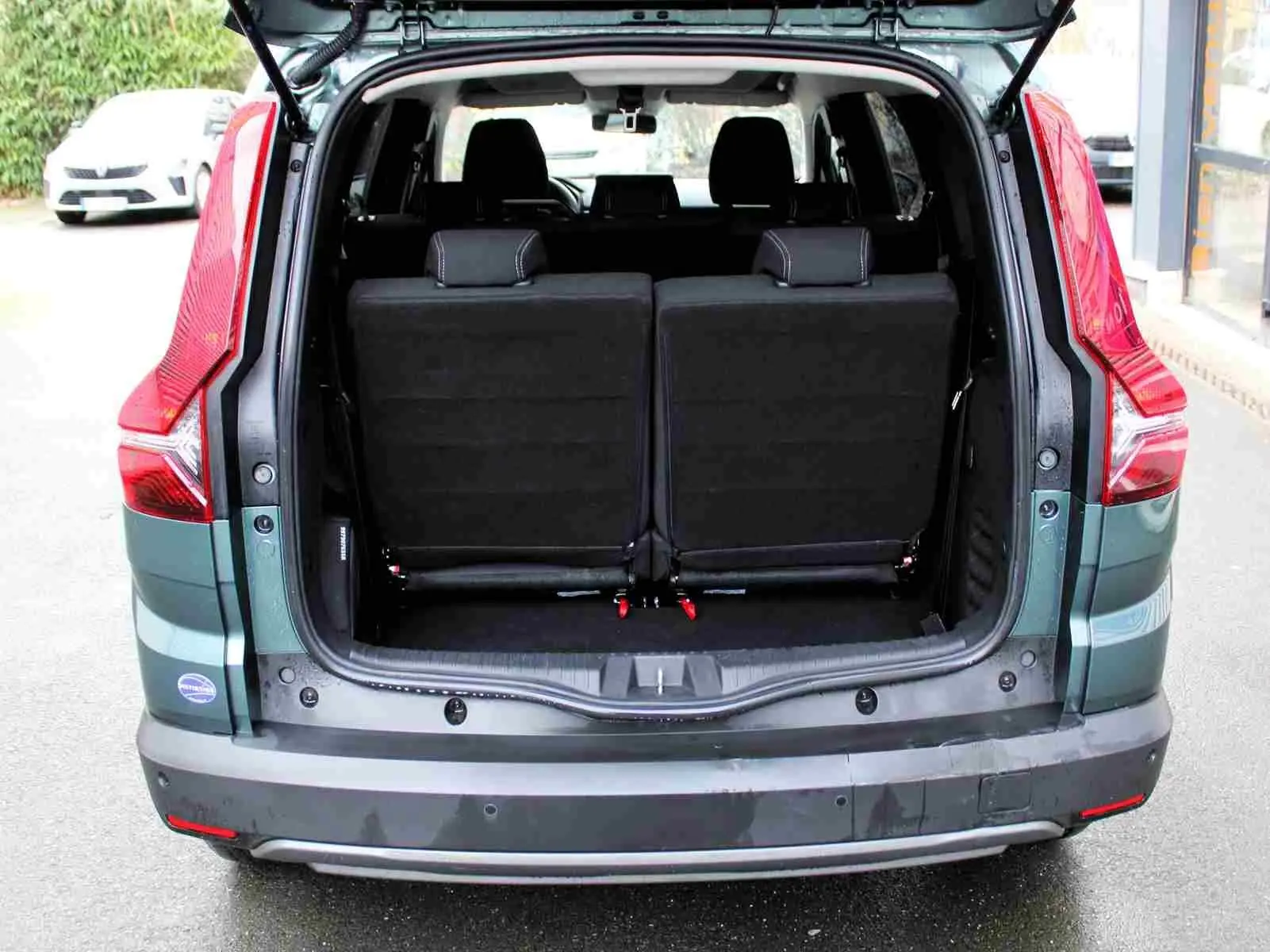Vue arrière du Dacia Jogger 2025 vert cèdre métal avec coffre ouvert et sièges rabattus visibles.
