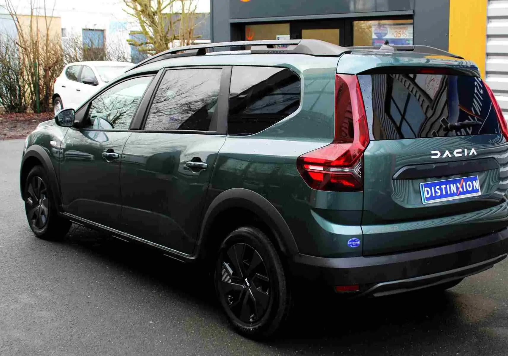 Vue 3/4 arrière gauche d'un Dacia Jogger vert cèdre métallisé avec feux arrière en forme de L et toit noir.