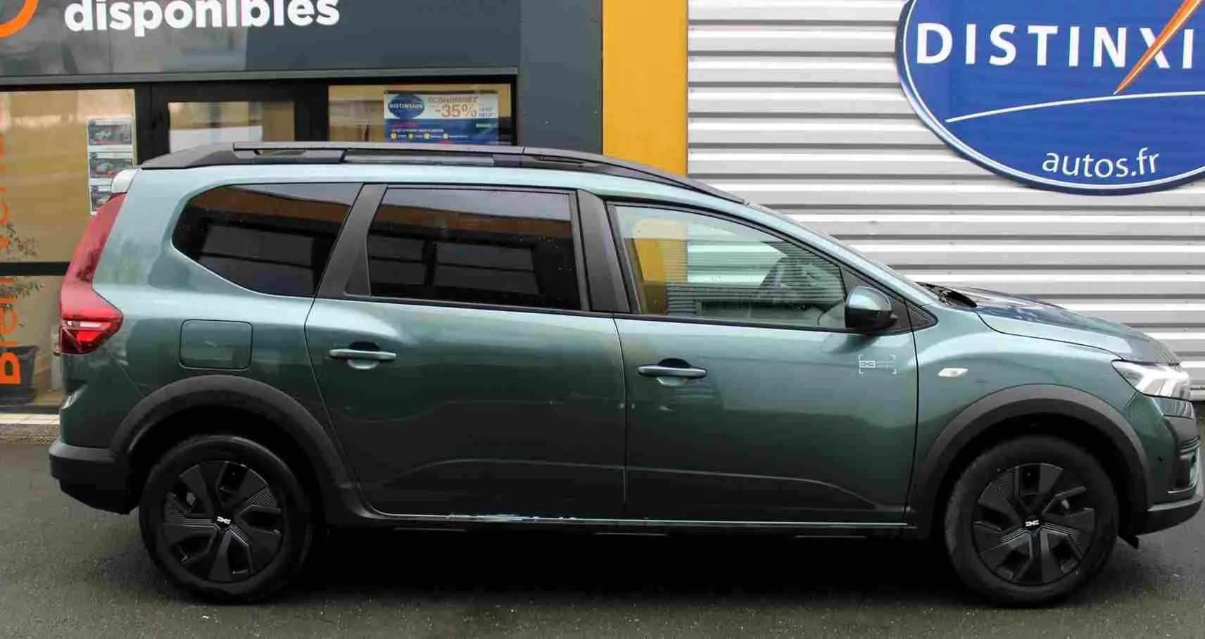 Vue de profil côté gauche d'un Dacia Jogger vert cèdre métallisé avec jantes noires et barres de toit.