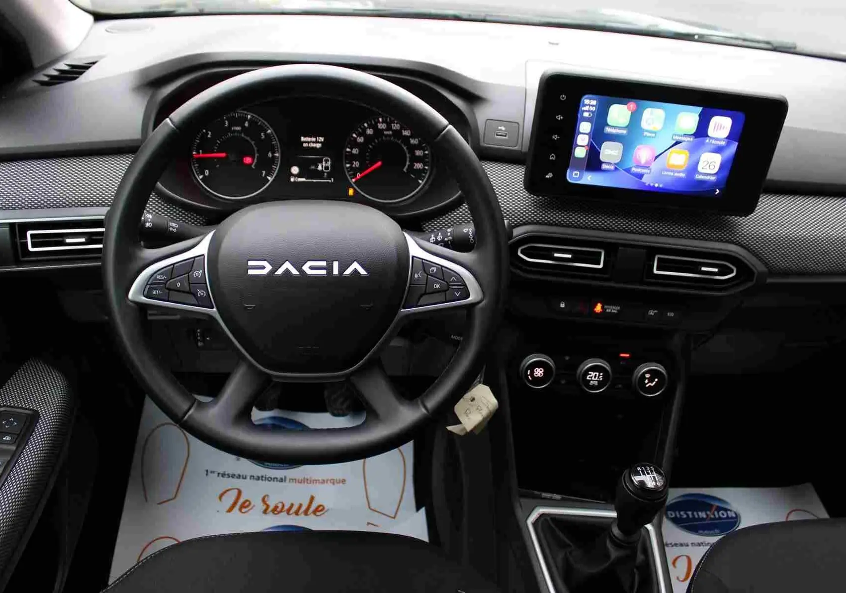 Vue intérieure frontale du tableau de bord du Dacia Jogger 2025, volant noir avec logo, écran tactile et levier de vitesses manuel.