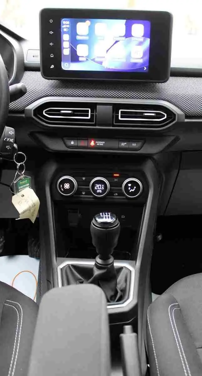 Vue intérieure centrée sur la console centrale d'une Dacia Jogger 2025, avec écran tactile, commandes climatisation et levier de vitesse manuel.