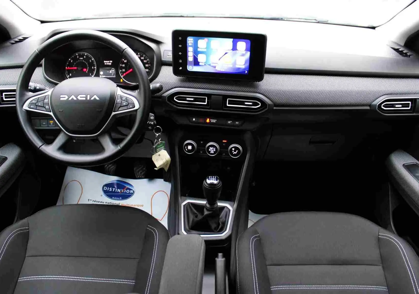 Vue intérieure avant du tableau de bord et volant de la Dacia Jogger 2025 avec écran tactile et levier de vitesse manuel.