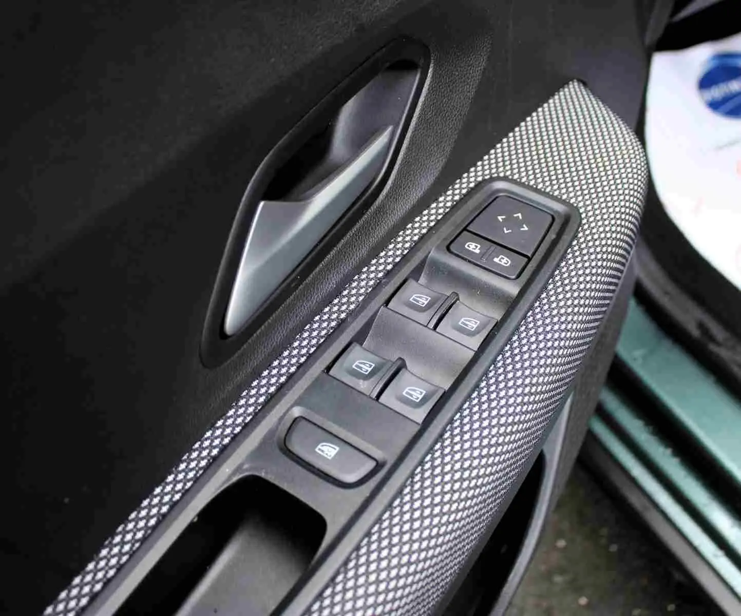 Gros plan sur la commande des vitres électriques côté conducteur du Dacia Jogger vert cèdre métal, avec poignée intérieure grise.