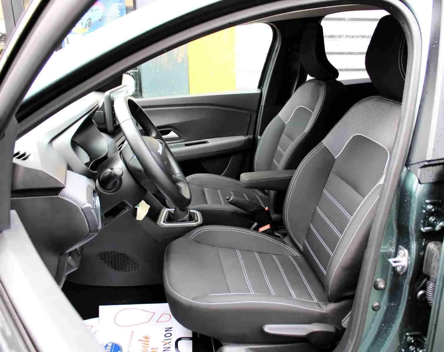 Vue intérieure côté conducteur du Dacia Jogger 2025 vert cèdre, montrant les sièges noirs et le volant multifonction.