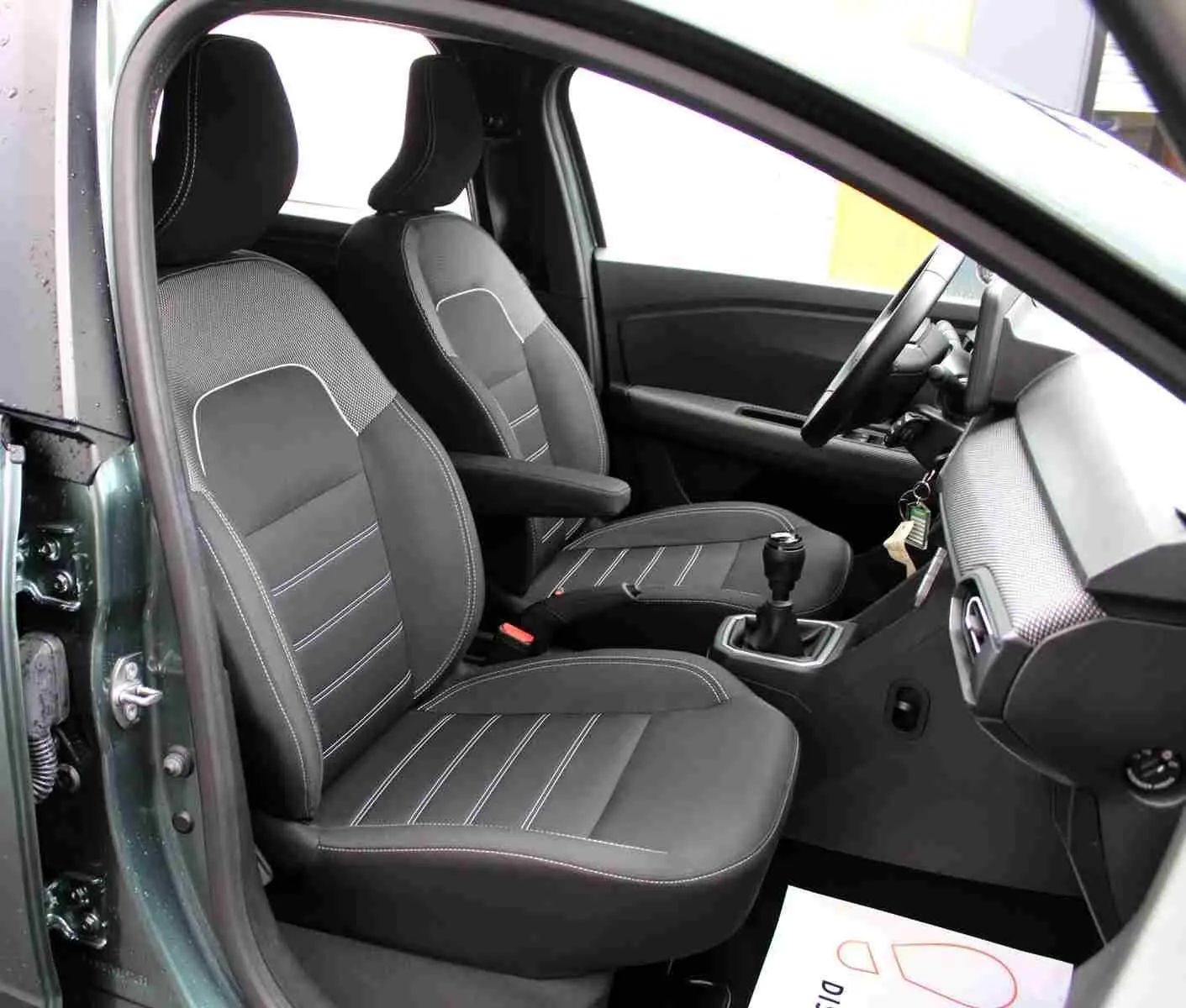 Vue intérieure côté gauche du Dacia Jogger 2025 vert cèdre, montrant les sièges avant noirs et la boîte manuelle.