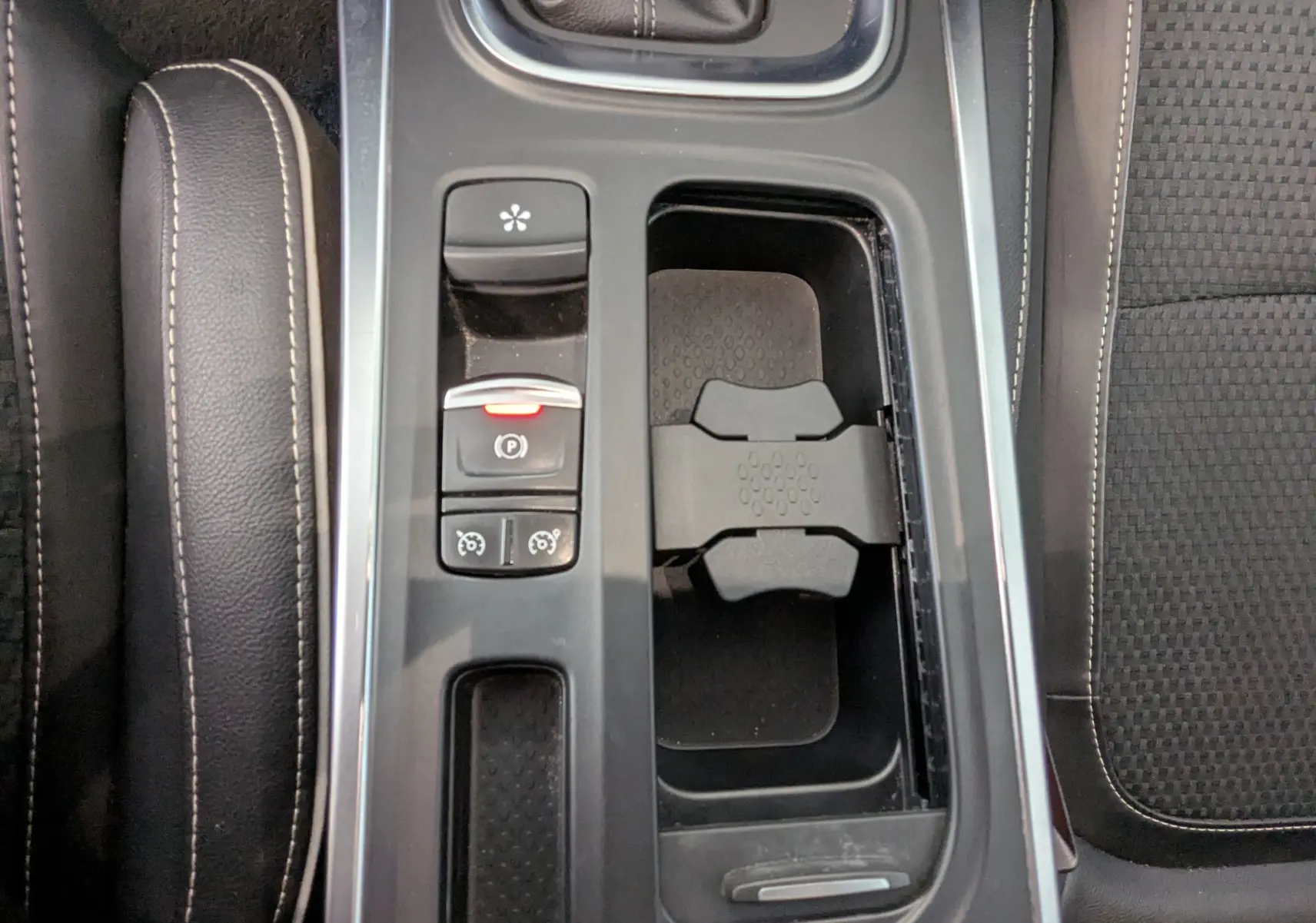 Vue plongeante sur la console centrale noire de la Renault Mégane IV gris, avec frein à main électronique et porte-gobelets.