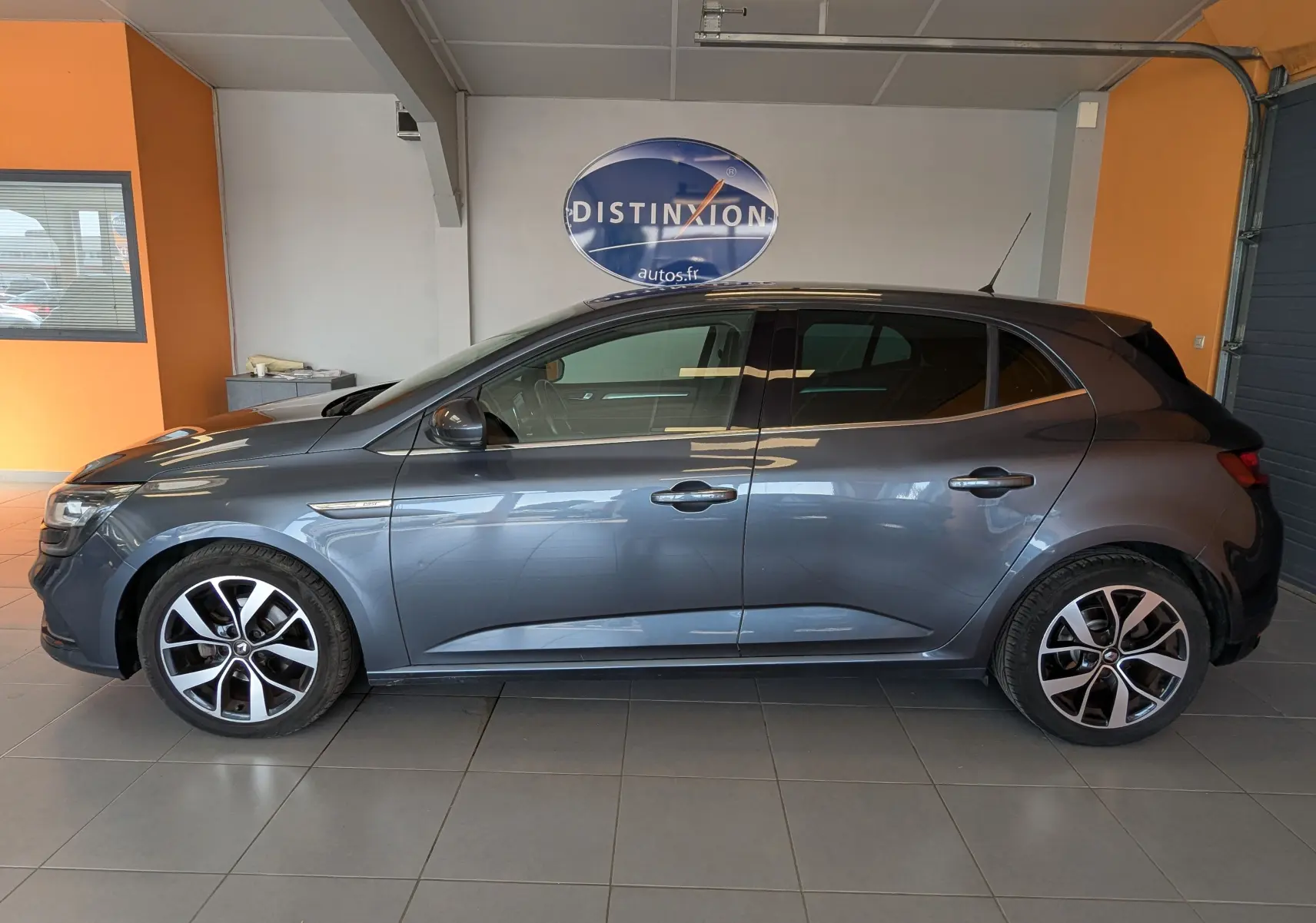 Renault Mégane IV gris vue de profil côté gauche, avec jantes alliage bi-ton et toit noir en intérieur showroom.