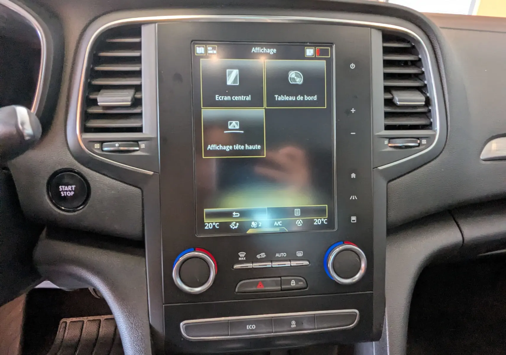 Vue rapprochée du tableau de bord noir de la Renault Mégane IV gris, avec écran tactile central et commandes climatisation.