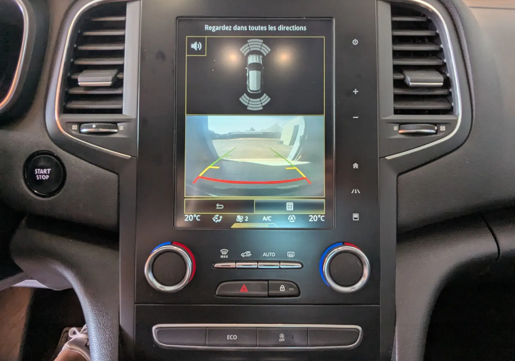 Vue rapprochée de la console centrale de la Renault Mégane IV gris, écran tactile affichant la caméra de recul et commandes climatisation.